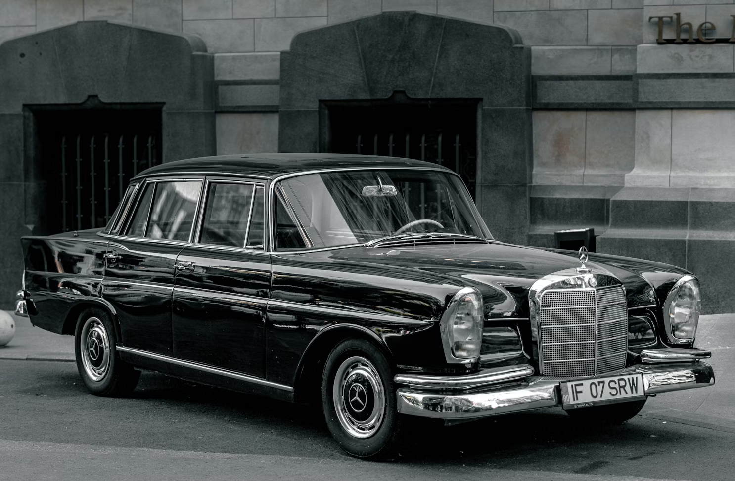 Classic black luxury sedan parked on a city street, featuring vintage design and chrome detailing.