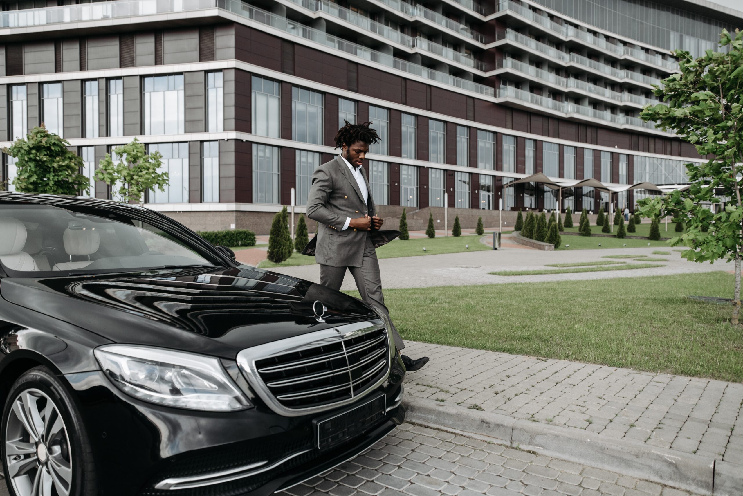 Chauffeur in suit outside Mercedes luxury car waiting at corporate office, executive travel service banner